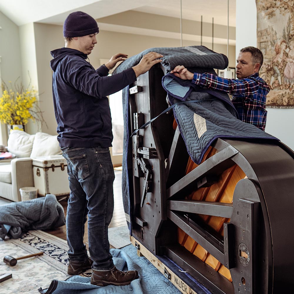 Professional movers packing a piano with protective moving blankets
